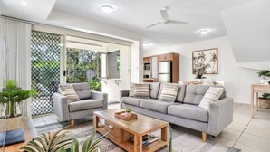 A modern living room with a grey sofa set, a wooden coffee table, and a ceiling fan. - Stylish Cairns Escape with Courtyard | Cosmo 14 (Cairns North)