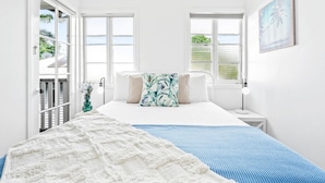 A bedroom with a bed, two windows, a nightstand, a lamp, and a painting. - Spacious 7-Bedroom Queenslander Retreat | Privacy, Comfort & Bushland Serenity (Aeroglen)