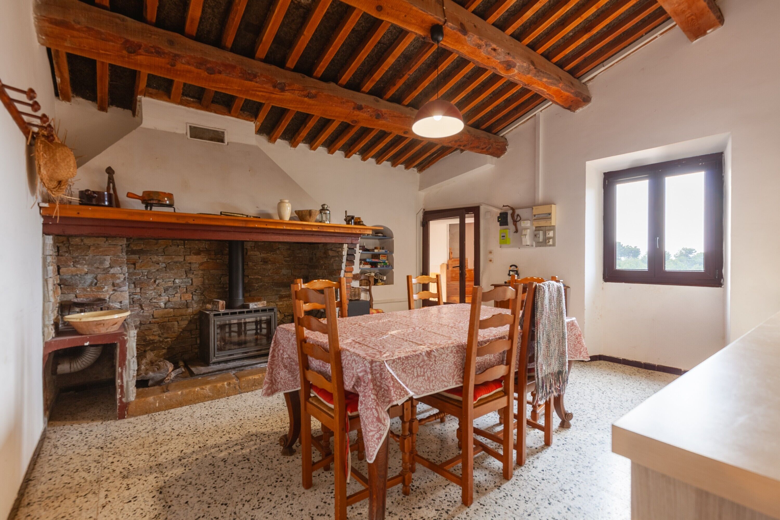 Zona pranzo rustica con camino in pietra, travi in legno al soffitto e tavolo apparecchiato per quattro persone.