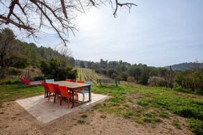 A patio with a table and chairs, a bench, and a view of a vineyard. - Holiday Home 'La Clavelle' with Mountain View, Private Terrace and Private Garden (Sanary-sur-Mer)