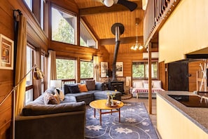 Un intérieur de chalet chaleureux avec une cheminée, un canapé, une table à manger et de grandes fenêtres.