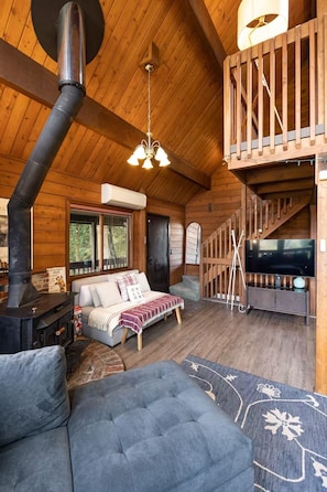 A cozy cabin interior with a fireplace, a sofa, a television, and a staircase.