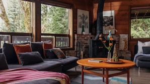 Un intérieur de chalet chaleureux avec une cheminée, de grandes fenêtres, un canapé et une table basse.