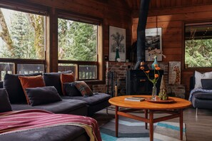 Un acogedor interior de cabaña con chimenea, ventanas amplias, un sofá y una mesa de centro.