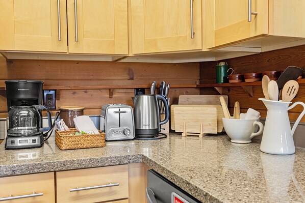 A kitchen with wooden cabinets, a granite countertop, a coffee maker, a toaster, a kettle, and various utensils.