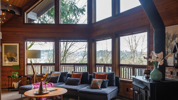 L’intérieur chaleureux d’un chalet avec un grand canapé en bois, une cheminée et de grandes fenêtres donnant sur le paysage extérieur.