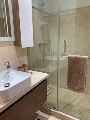 A modern bathroom with a glass-enclosed shower, a white sink, and a wooden vanity.