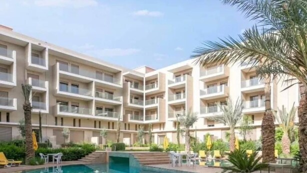 Un hôtel à plusieurs étages doté d’une piscine centrale, entourée de palmiers et agrémentée d’un espace salon extérieur.