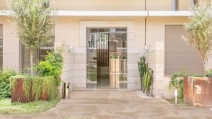 Une entrée moderne, avec une porte en verre, un chemin en béton et de la verdure environnante.