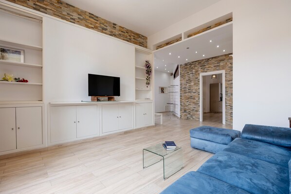 A modern living room with a blue sofa, a glass coffee table, and a flat-screen TV.