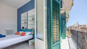 Une chambre à coucher avec un lit, une porte-fenêtre coulissante, un balcon avec une balustrade et une vue sur le paysage urbain.