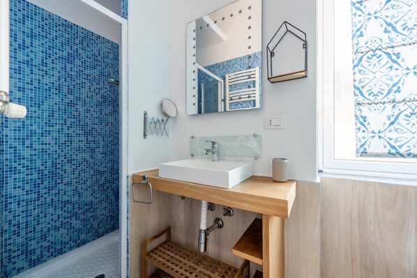 A bathroom with a blue mosaic tile wall, a white sink, a wooden vanity, a mirror with a decorative frame, and a patterned window view.