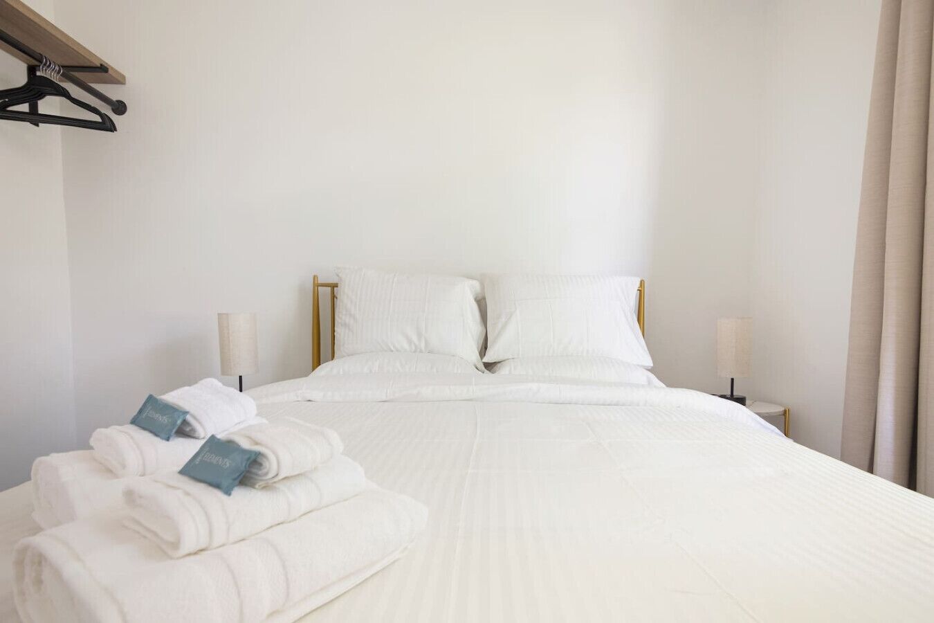 Una cama bien tendida con sábanas blancas, cabecera de madera y dos lámparas de noche.