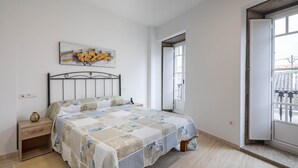 Un dormitorio con una cama, una mesita de noche, una obra de arte en la pared y una puerta que da a un área exterior.