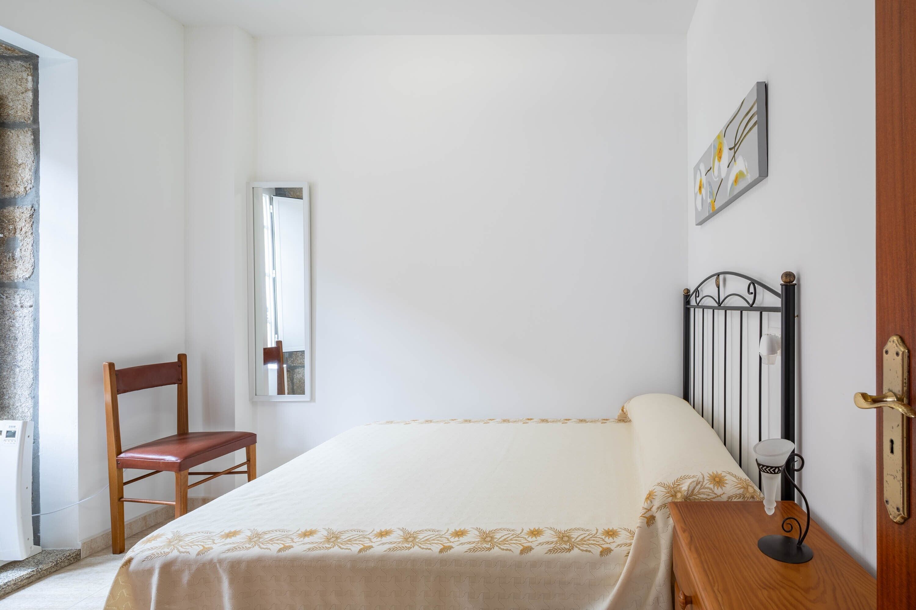 Ein Schlafzimmer mit einem Bett, einem Sessel, einem Nachttisch, einem Spiegel und einer Tür.