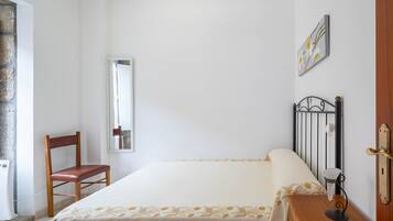 Ein Schlafzimmer mit einem Bett, einem Sessel, einem Nachttisch, einem Spiegel und einer Tür.
