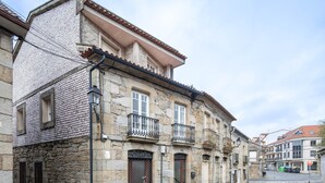 Un edificio histórico de piedra con tejado de tejas, varias ventanas y una calle adoquinada.