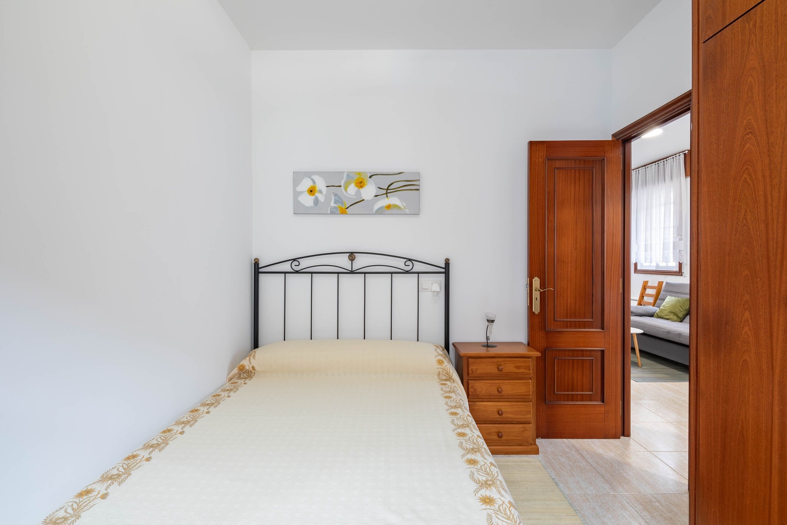 Un dormitorio con cama, mesita de noche, armario de madera y un cuadro en la pared.