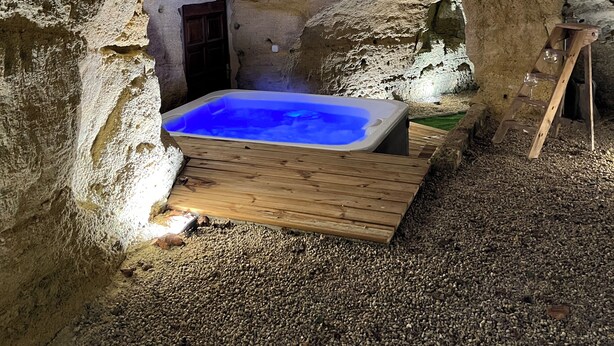 Una vasca idromassaggio immersa in una struttura simile a una grotta, con un pontile in legno e una piccola porta.