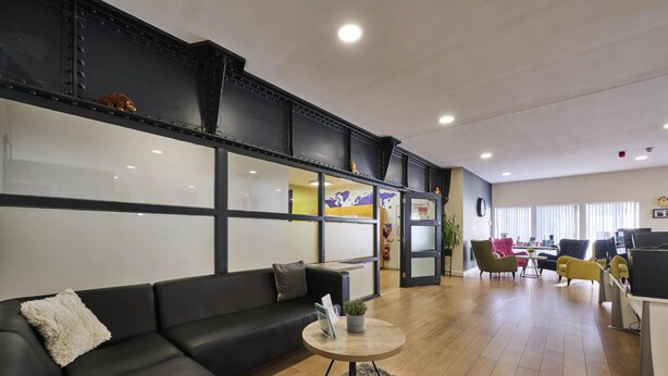 A modern hotel lobby with a black leather sofa, a round wooden table, and colorful chairs. - Upperton Road Studios in Leicester (Leicester)