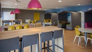 A modern dining area with wooden tables and chairs, pink pendant lights, and a blue accent wall. - Upperton Road Studios in Leicester (Leicester)