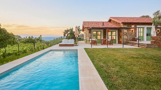 Zona de piscina con una casa de piedra, mobiliario exterior y vistas al viñedo.