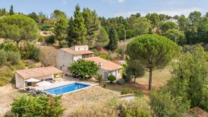 A villa with a swimming pool, surrounded by trees and a hilly landscape.