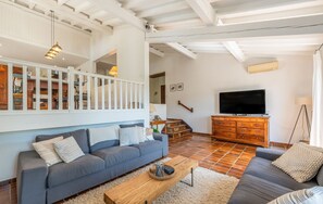 Un salón amplio con un sofá gris, una mesa de centro de madera y un televisor sobre un mueble de madera.