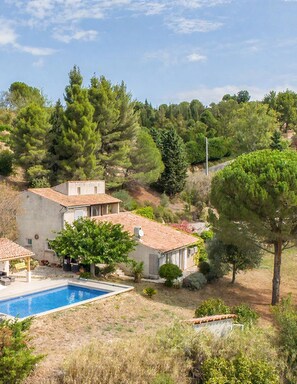 A house with a swimming pool, surrounded by trees and a hilly landscape.