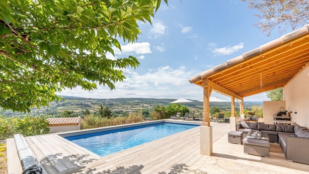 A pool with a wooden deck, outdoor furniture, and a pergola.