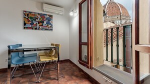 A room with a dining table and chairs, a window with a view of a dome and buildings, and a colorful abstract painting on the wall.