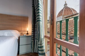 A bedroom with a bed, a nightstand, a lamp, and a view of a dome and tiled roof through a window. - Apartment 'Calzaiuoli 10 - Boutique' with Wi-Fi and Air Conditioning (Firenze)