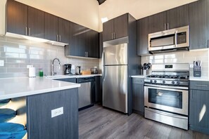 Une cuisine moderne dotée d’appareils électroménagers en acier inoxydable, de meubles de rangement aux couleurs sombres et d’un plan de travail blanc.