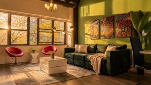 Una sala de estar moderna con una pared verde, ventanas amplias, un sofá verde, sillas rojas y obras de arte.