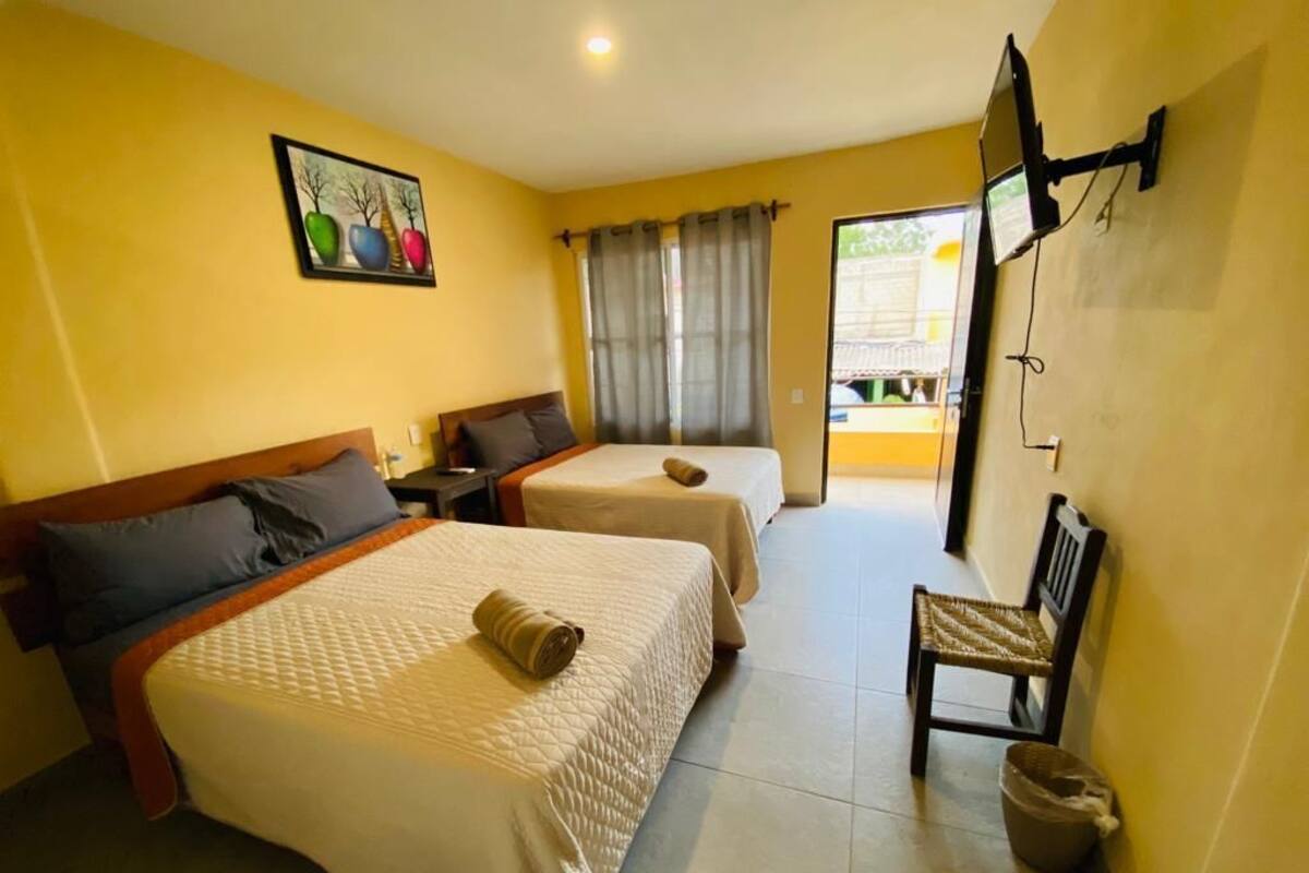 A hotel room with two beds, a TV, a chair, and a window with curtains.