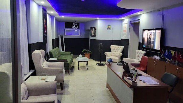 A modern reception area with a reception desk, seating area with sofas and armchairs, a television, and a ceiling with blue lighting.