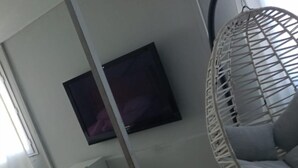 A room with a white fan chair, a flat-screen TV mounted on the wall, and a tiled floor.