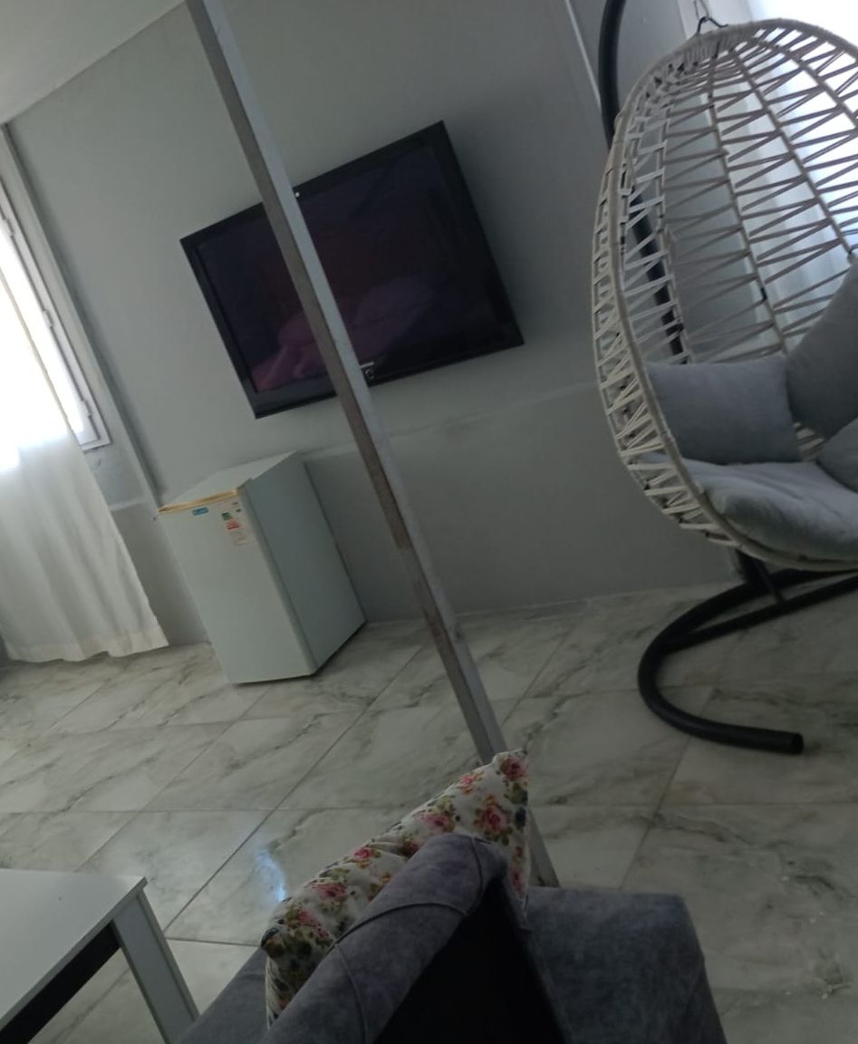 Ein Zimmer mit weißem Fächerstuhl, einem an der Wand montierten Flachbildfernseher und einem Fliesenboden.