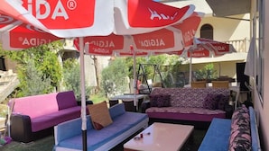 An outdoor seating area with two sofas, a coffee table, and a swing chair under red and white umbrellas.