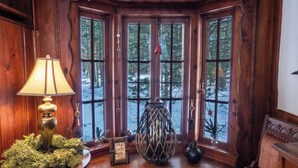 A cozy corner with a wooden bench, a lamp, and a window with a view of a snowy forest. - Enchanted Fox Dell Cottage (Smallwood)
