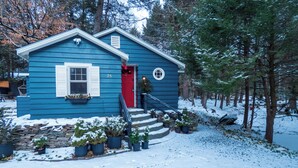 A blue house with a red door, surrounded by snow and trees. - Enchanted Fox Dell Cottage (Smallwood)