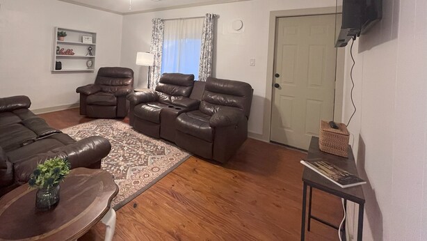 Ein Wohnzimmer mit Deckenventilator, zwei Ledersofas, einem Couchtisch, einem an der Wand befestigten Fernseher und einer Tür.