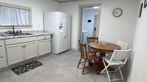 Eine kompakte Küche mit weißen Schränken, einem eingebauten Kühlschrank, einer Spüle und einem Essbereich mit Holztisch und Stühlen.