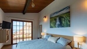Ein Schlafzimmer mit Bett, Fernseher, einem Gemälde und Blick durch eine Schiebetür.