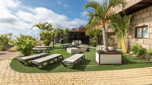 Eine Terrasse mit Sitzgelegenheiten im Freien, Palmen und einem Gebäude mit Steinmauern.