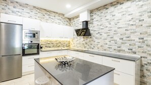 Eine moderne Küche mit Kochinsel, integriertem Backofen, Edelstahlkühlschrank und Spritzschutz mit Steinmuster.