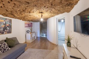 Ein modernes Wohnzimmer mit Steindecke, einem grauen Sofa, einem weißen Schrank, einem Flachbildfernseher und einer Duschkabine aus Glas.