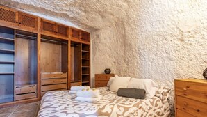 A bedroom with a bed, wooden wardrobe, and a stone wall. - Vacation Home 'Añaterve' with Sea View, Private Pool and Wi-Fi (Arico)