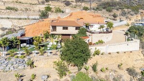Una propiedad en una ladera con una casa de piedra, un patio con mobiliario exterior y un pequeño jardín.