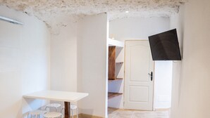 Una habitación con una mesa y sillas blancas, suelo de madera, una puerta blanca y un televisor montado en la pared.
